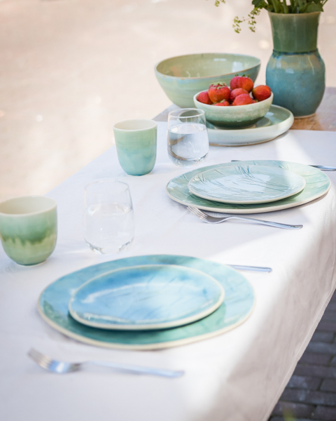 Gedekte tafel met blauwgroene keramische borden, bekers en een kom aardbeien